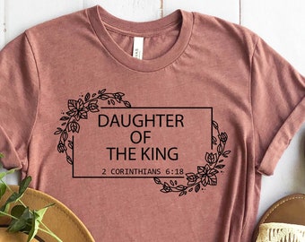 Może przedstawiać: Koszulka w kolorze malwy z kwiatowym wzorem i nadrukiem "Daughter of the King 2 Corinthians 6:18" z przodu.
