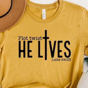 May include: A mustard yellow t-shirt with a black cross and the text "Plot twist HE LIVES Luke 24:23".