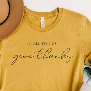 May include: A mustard yellow t-shirt with the text "In all things give thanks" in black script.