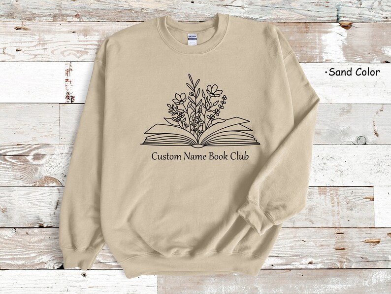 May include: A sand-colored sweatshirt with a black outline of an open book with flowers growing out of it. The text "Custom Name Book Club" is printed below the book.