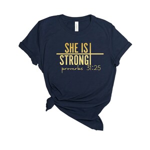 May include: Navy blue t-shirt with gold lettering that reads "She is Strong" and "Proverbs 31:25".