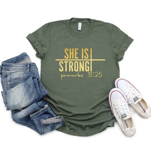 May include: A green t-shirt with the text "She is Strong" and "Proverbs 31:25" in gold lettering.