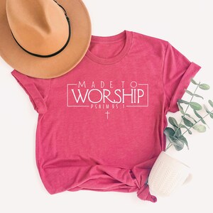 Puede incluir: Una camiseta rosa con el texto "MADE TO WORSHIP - PSALM 95:1" en letras blancas. La camiseta tiene una cruz blanca debajo del texto.