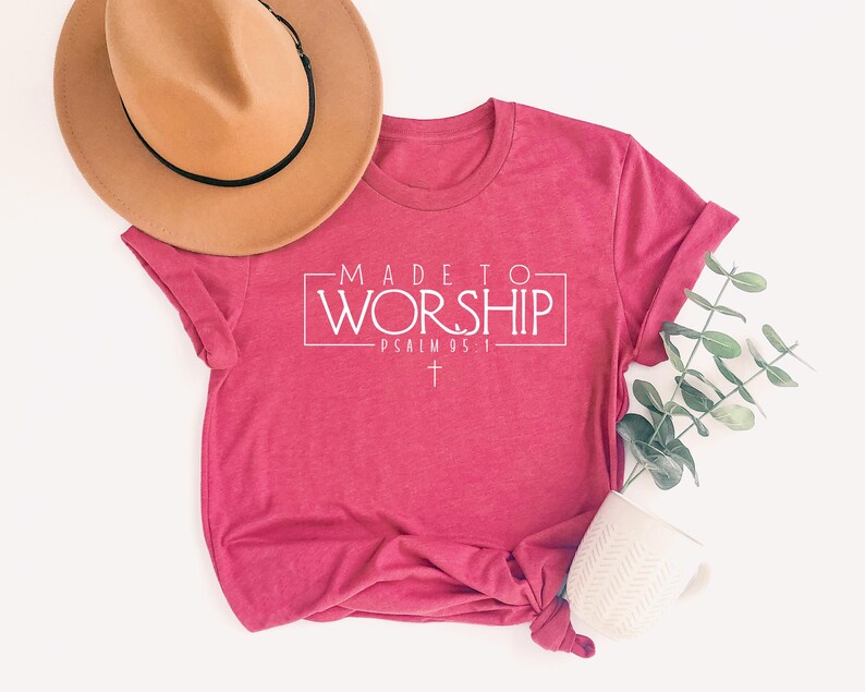 Puede incluir: Una camiseta rosa con el texto "MADE TO WORSHIP - PSALM 95:1" en letras blancas. La camiseta tiene una cruz blanca debajo del texto.