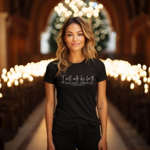 May include: A black t-shirt with the text "I will walk by faith, even when I cannot see, 2 Corinthians 5:7" in white script. The shirt is worn by a person in a church setting.