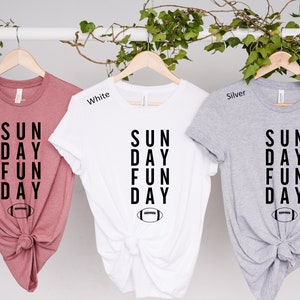 Pu&ograve; includere: Tre magliette in malva, bianco e argento con il testo "SUN DAY FUN DAY" e una grafica di un pallone da calcio.
