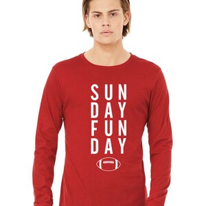 Pu&ograve; includere: Maglietta a maniche lunghe rossa con testo bianco che recita "SUNDAY FUN DAY" e una grafica di un pallone da calcio bianco.