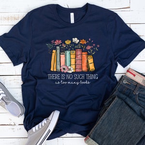 May include: Navy blue t-shirt with a stack of colorful books and flowers. The text on the shirt reads "There is no such thing as too many books."