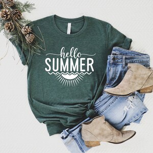 May include: A green t-shirt with the text "hello summer" in white lettering. The shirt is styled with blue jeans and brown ankle boots.