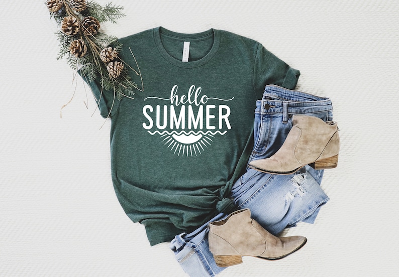 May include: A green t-shirt with the text "hello summer" in white lettering. The shirt is styled with blue jeans and brown ankle boots.
