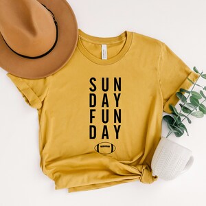 Pu&ograve; includere: Una maglietta color senape con il testo "SUN DAY FUN DAY" e un'immagine di un pallone da calcio.