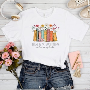 May include: White t-shirt with a graphic of a stack of colorful books with flowers on top. The text "THERE IS NO SUCH THING as too many books" is printed below the graphic.