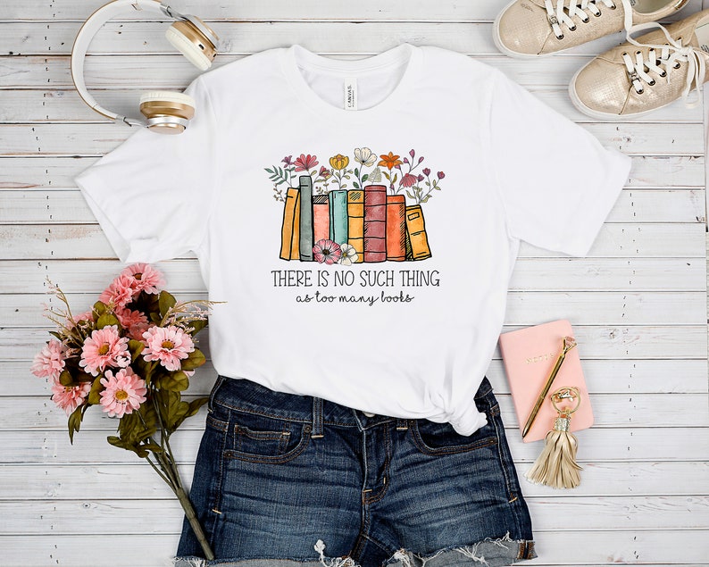 May include: White t-shirt with a graphic of a stack of colorful books with flowers on top. The text "THERE IS NO SUCH THING as too many books" is printed below the graphic.