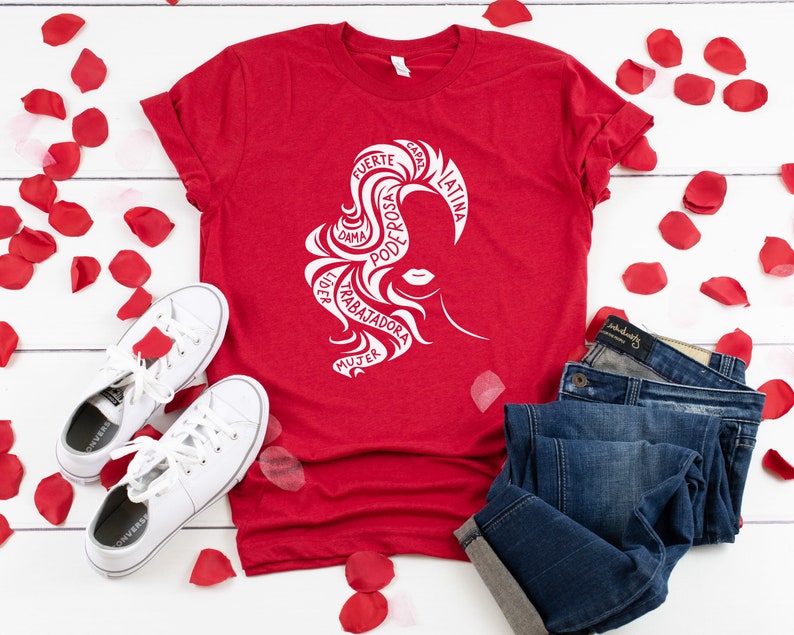 May include: Red t-shirt with a white silhouette of a woman's head with the words "FUERTE, CAPAZ, LATINA, PODEROSA, DAMA, LIDER, TRABAJADORA, MUJER" in a circle around her head.