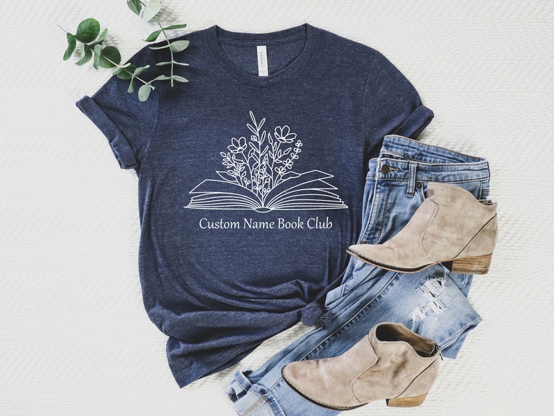 May include: A navy blue t-shirt with a white outline of an open book with flowers growing out of it. The text "Custom Name Book Club" is printed below the book.