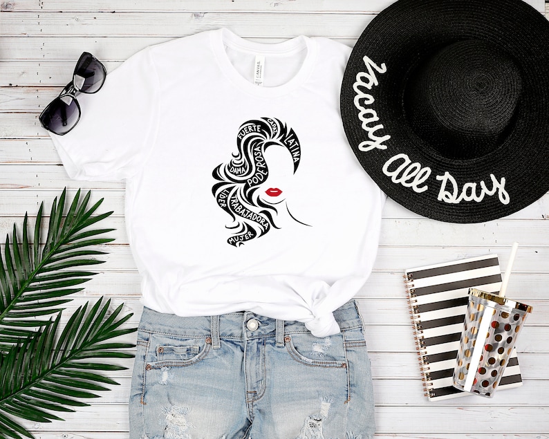 May include: White t-shirt with a black and red graphic of a woman's face with the words "fuerte", "poderosa", "guerrera", "trabajadora", "mujer", "dama", "unica", "latina" written in her hair.
