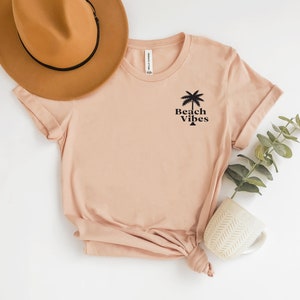 May include: A light pink t-shirt with a palm tree and the text "Beach Vibes" printed on the front.