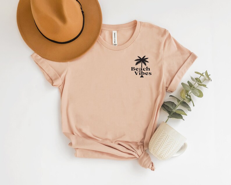 May include: A light pink t-shirt with a palm tree and the text "Beach Vibes" printed on the front.