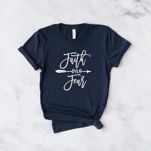May include: A navy blue t-shirt with the text "Faith over Fear" in white lettering with a white arrow and feather design.