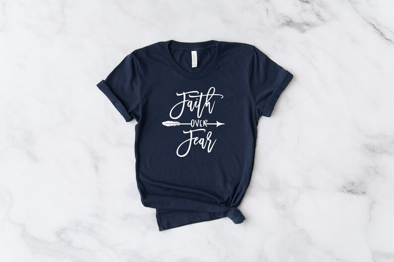 May include: A navy blue t-shirt with the text "Faith over Fear" in white lettering with a white arrow and feather design.