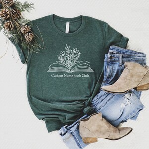 May include: A dark green t-shirt with a white outline of an open book with flowers growing out of it. The text "Custom Name Book Club" is printed below the book.