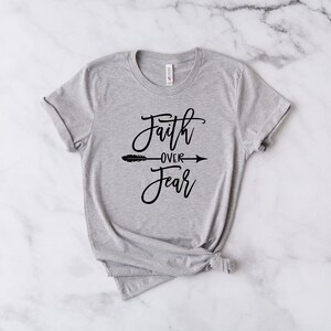 May include: A gray t-shirt with the text "Faith over Fear" in black script with an arrow pointing to the right.
