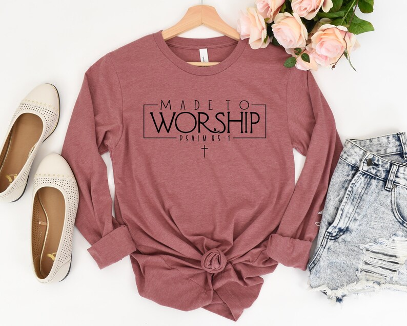 Puede incluir: Una camiseta de manga larga de color granate con el texto "MADE TO WORSHIP - PSALM 95:1" impreso en la parte delantera. Una peque&ntilde;a cruz se encuentra debajo del texto.