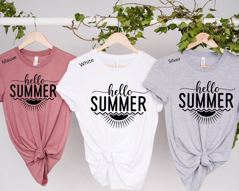 May include: Three t-shirts with the text "hello summer" in black lettering on a white background. The t-shirts are displayed on hangers and are in the colors mauve, white, and silver.