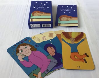 Könnte beinhalten: Ein Orakelkarten-Deck mit einer blauen Box und einem Booklet, beide mit dem Text "Oracle Wisdom Cards" und einer Illustration einer schlafenden Person. Mehrere Karten werden angezeigt, jede mit farbenfrohen Illustrationen und Zahlen.