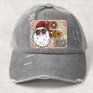 May include: A gray distressed trucker hat with a patch featuring a cartoon Santa Claus wearing sunglasses and a peace sign. The patch has a floral background with the text "Ho Ho Ho" in a retro font.