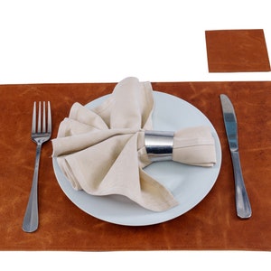 May include: A brown leather placemat with a white plate, a white napkin, a silver napkin ring, a fork, and a knife.