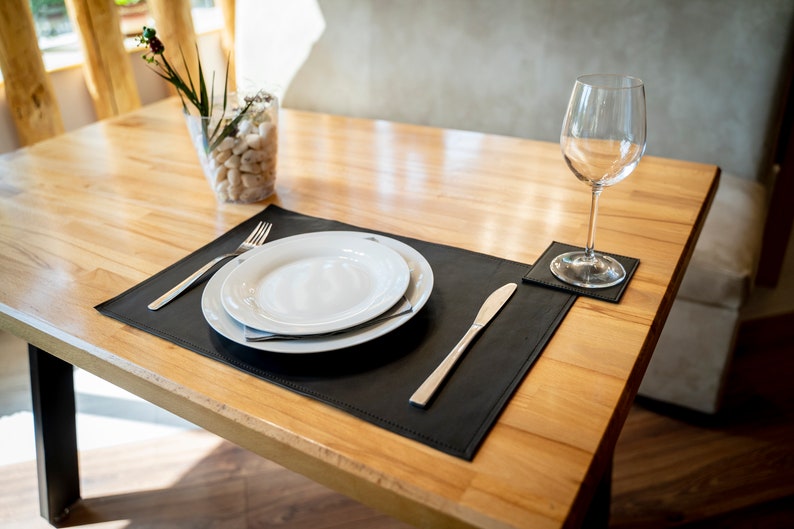 May include: A black leather placemat with a white plate, fork, and knife. A glass of water sits on a matching leather coaster.