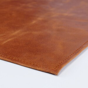 May include: A close-up of a brown leather placemat with a stitched edge.