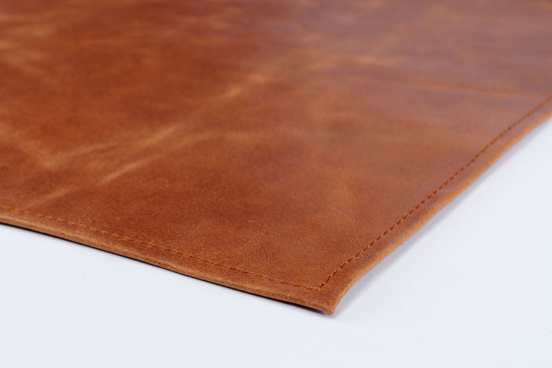May include: A close-up of a brown leather placemat with a stitched edge.