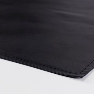 May include: A close-up of a black fabric with a stitched edge. The fabric is smooth and appears to be made of a durable material.