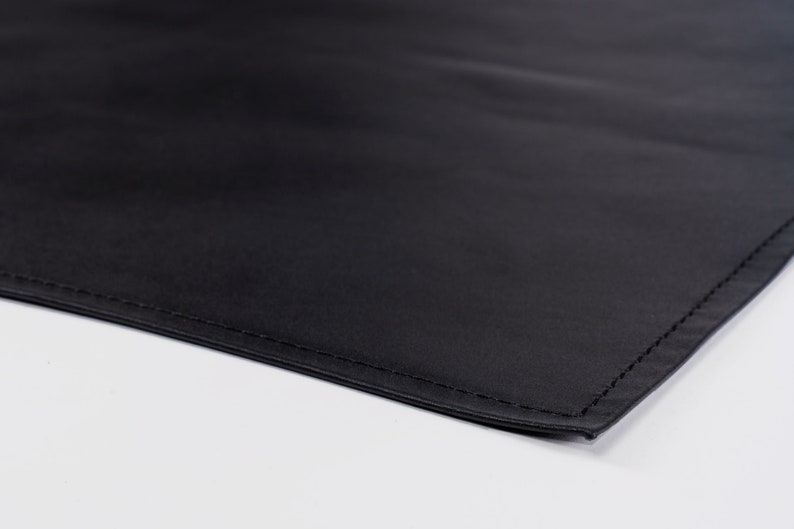 May include: A close-up of a black fabric with a stitched edge. The fabric is smooth and appears to be made of a durable material.