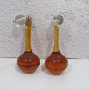 May include: A pair of amber glass bottle stoppers with clear glass ball tops. The stoppers have a thin, dark line around the bottom of the bulb.