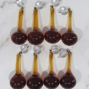 May include: Eight amber glass teardrop chandelier crystals with clear glass tops and gold metal accents.