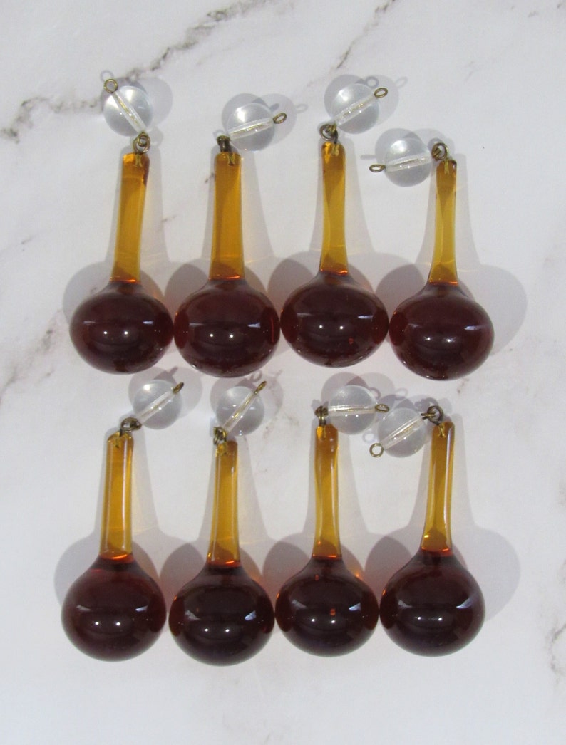 May include: Eight amber glass teardrop chandelier crystals with clear glass tops and gold metal accents.