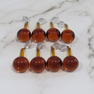 May include: Eight amber glass chandelier prisms with clear glass beads. The prisms are teardrop shaped with a round bottom and a pointed top.