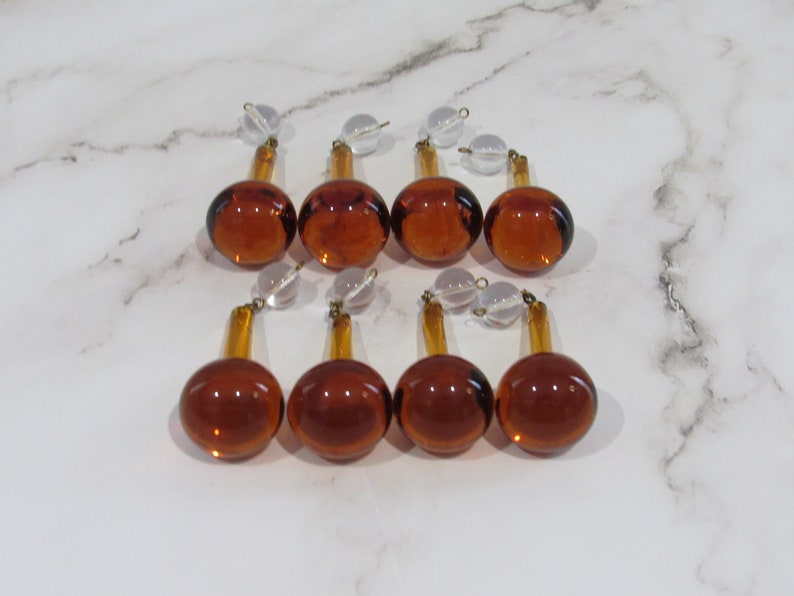 May include: Eight amber glass chandelier prisms with clear glass beads. The prisms are teardrop shaped with a round bottom and a pointed top.