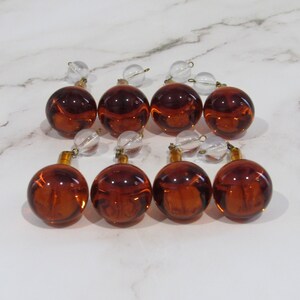 May include: Eight amber glass ornaments with clear glass beads and gold accents. The ornaments are arranged in two rows of four.