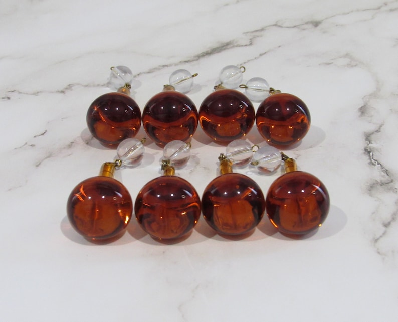 May include: Eight amber glass ornaments with clear glass beads and gold accents. The ornaments are arranged in two rows of four.