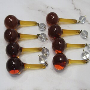 May include: Ten amber glass teardrop chandelier prisms with clear crystal connectors. Each prism has a round bulb and a long, thin stem.