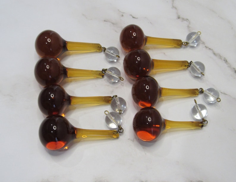 May include: Ten amber glass teardrop chandelier prisms with clear crystal connectors. Each prism has a round bulb and a long, thin stem.