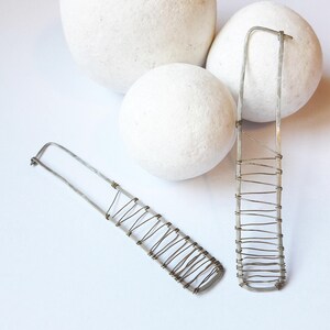 May include: A pair of silver earrings with a geometric design. The earrings are made of thin wire that is wrapped around a rectangular frame.