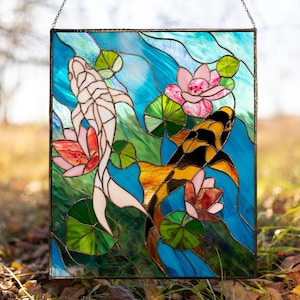 May include: A stained glass window panel depicting two koi fish swimming in a pond with lily pads and flowers. The fish are a white koi and a black and orange koi. The background is a blue and green water pattern.