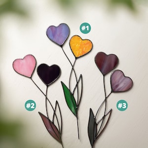 Op de afbeelding: Drie glas-in-lood hartvormige bloemdecoraties met verschillende gekleurde glazen harten. De harten zijn paars, roze, oranje en bruin. De bloemen zijn genummerd 1, 2 en 3.