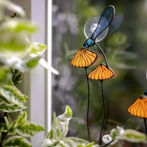 suncatcher in the form of two orange mushrooms with veins on which sits a dragonfly with blue wings in a plant vase. dragonfly stain glass
