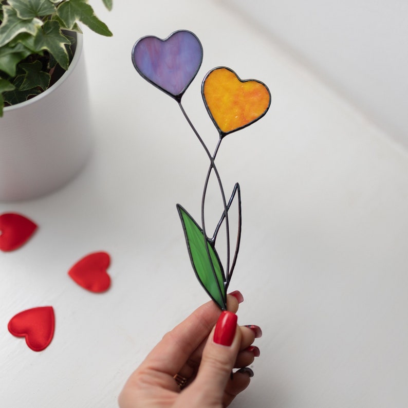 Op de afbeelding: Een boeket van hartvormige bloemen van gekleurd glas met paarse en oranje harten en een groen blad.